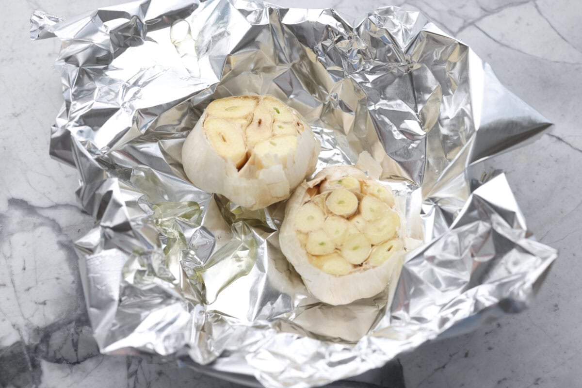 Every time I make garlic bread, my family eats every last piece! This garlic bread pasta has all the same buttery, garlicky flavor you love, just in pasta form. It’s creamy, comforting, and easy to make! And there is plenty to go around! two garlic bunches with tops cute off in tin foil ready to be roasted.