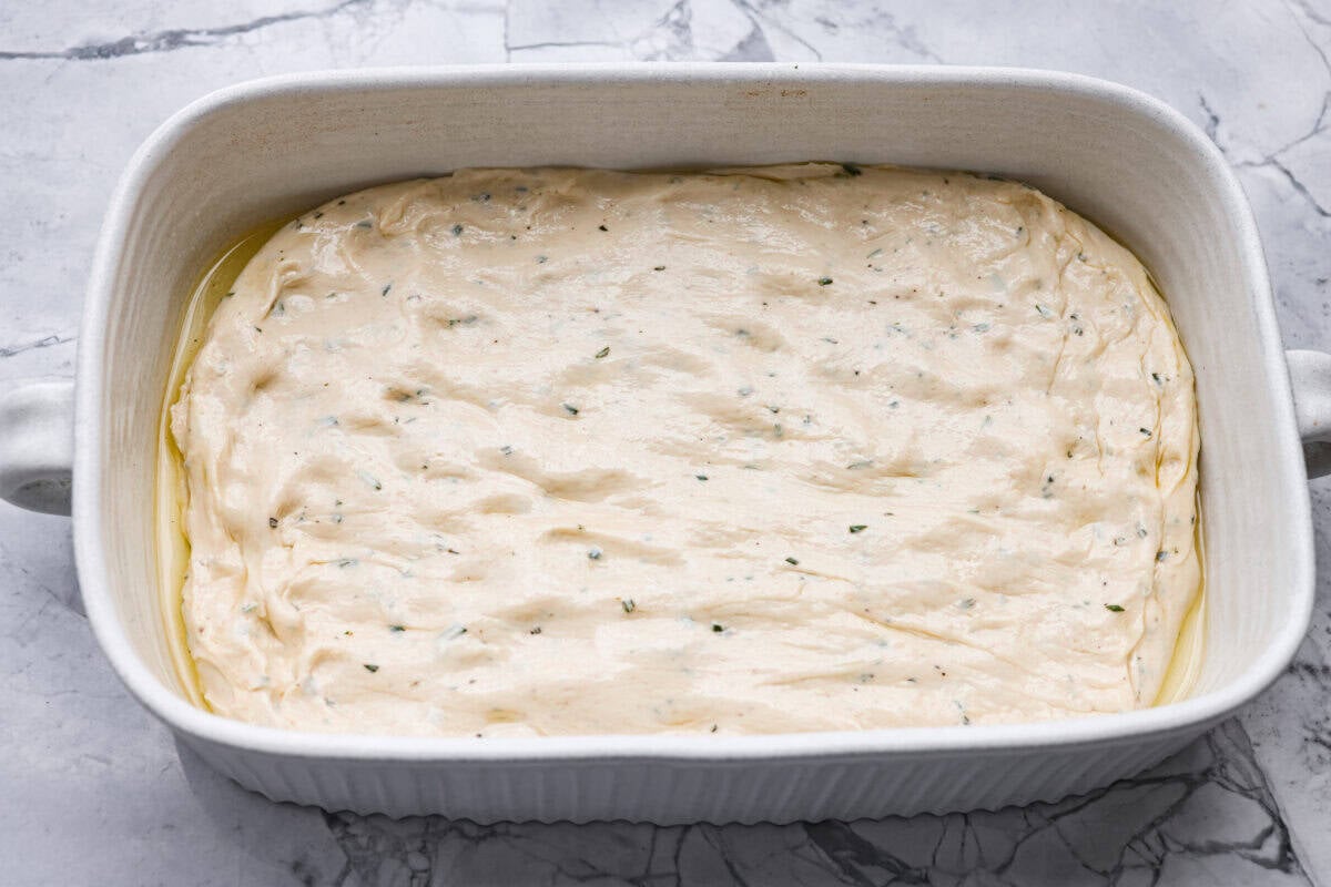 Focaccia dough spread out in a baking with olive oil. 