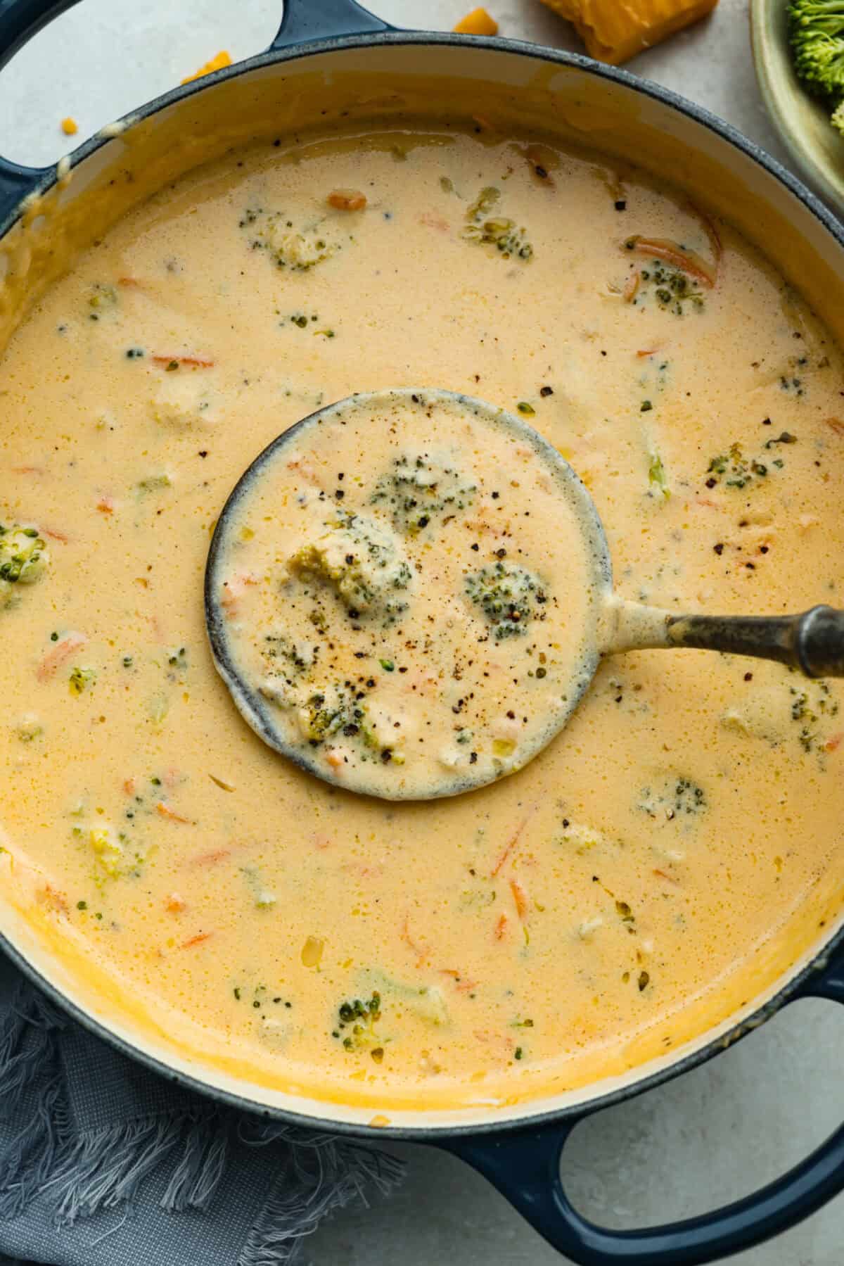 I promise that with just one bite of this copycat Panera Bread Broccoli Cheddar Soup, you'll be hooked! It's ultra creamy with broccoli, shredded carrots, and a hint of nutmeg, all cooked together with melted cheese. This soup is delicious and easy to make! Overhead shot of Panera broccoli cheddar soup in a pot with a ladel.