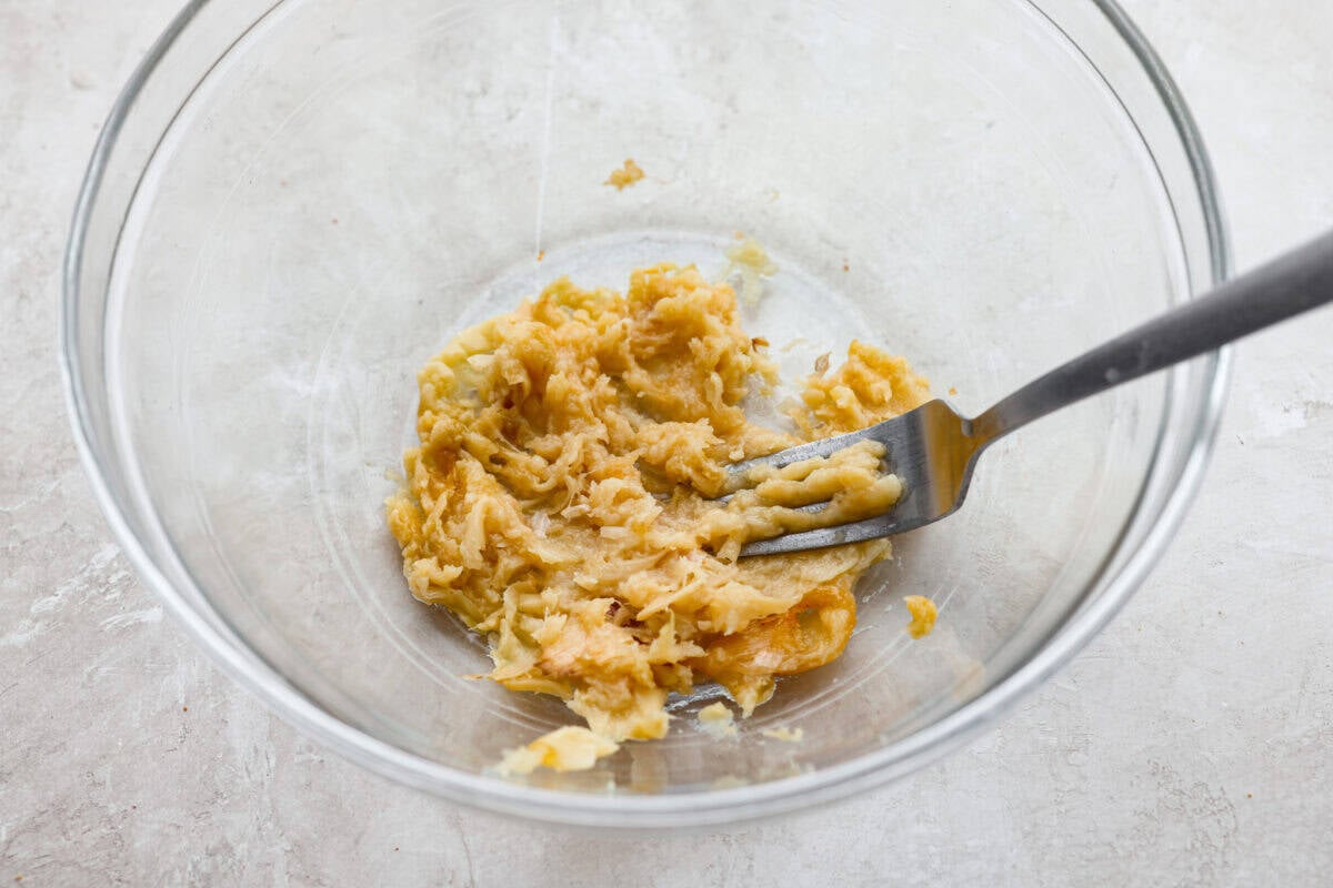 Cheesy garlic bread made into the dip of your dreams! This Garlic Bread Dip is full of roasted garlic and layers of melty cheese. It's irresistible from the very first bite! Roasted garlic being smashed into a paste.