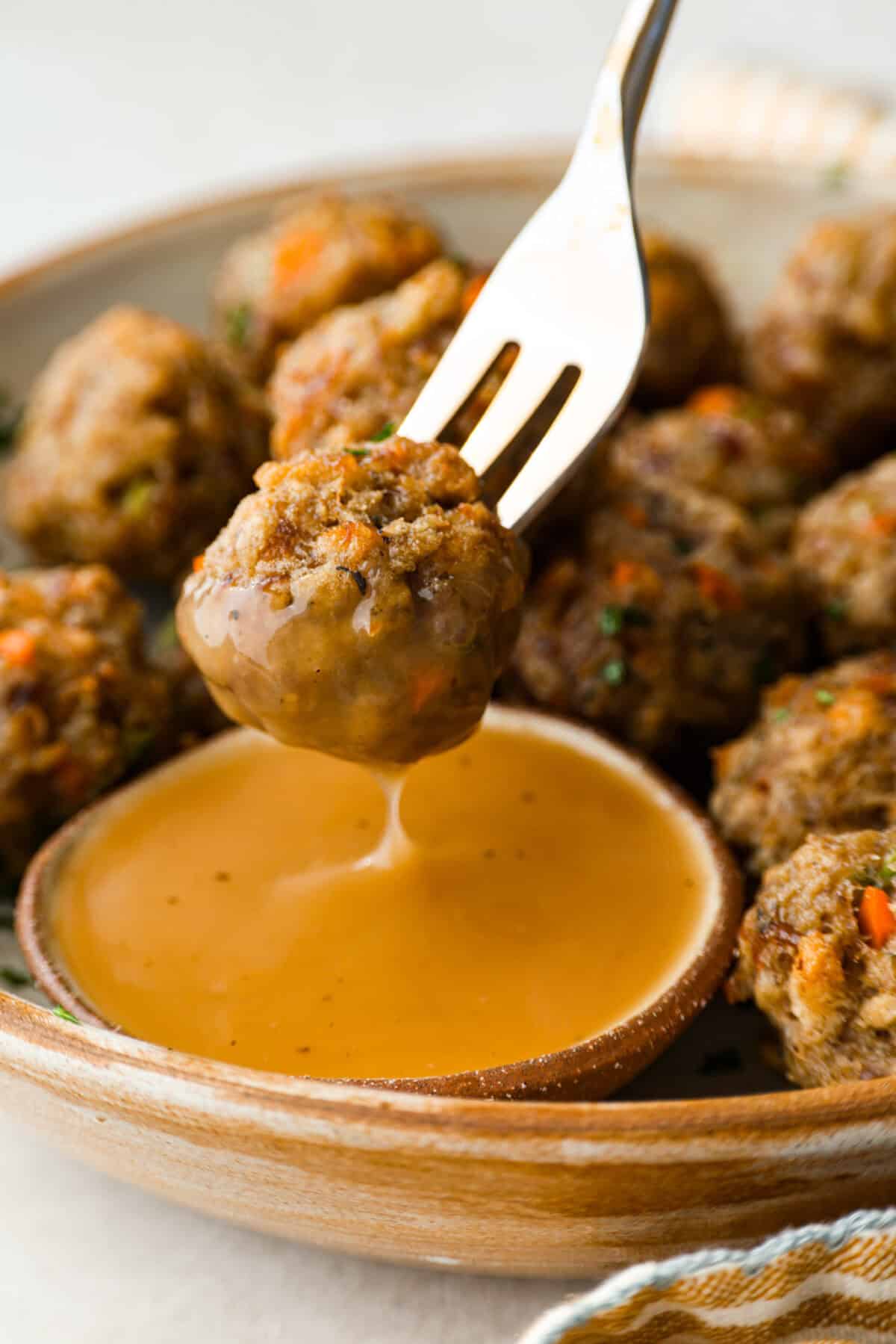 I'm telling you guys right now, sausage stuffing balls are the best part of my holiday table. They're crispy on the outside, soft and savory on the inside, and loaded with classic stuffing flavor. Easy to make, fun to share, and they disappear fast. Someone dipping a sausage ball into some gravy.