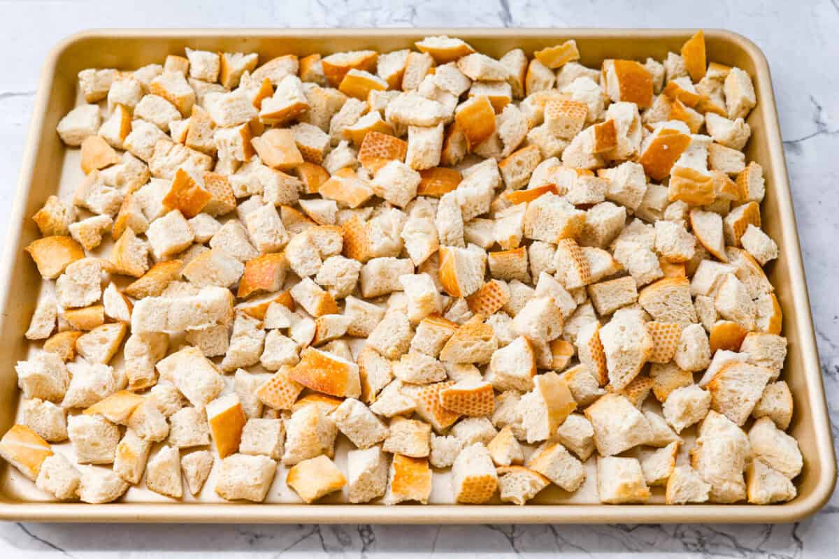 Why did it take me this long to use it in stuffing? Sourdough Stuffing's tangy crust and the chewy middle are perfection! Every bite soaks up all that buttery, herby goodness like it was made for this. Cubed sourdough bread on a cookie tray.