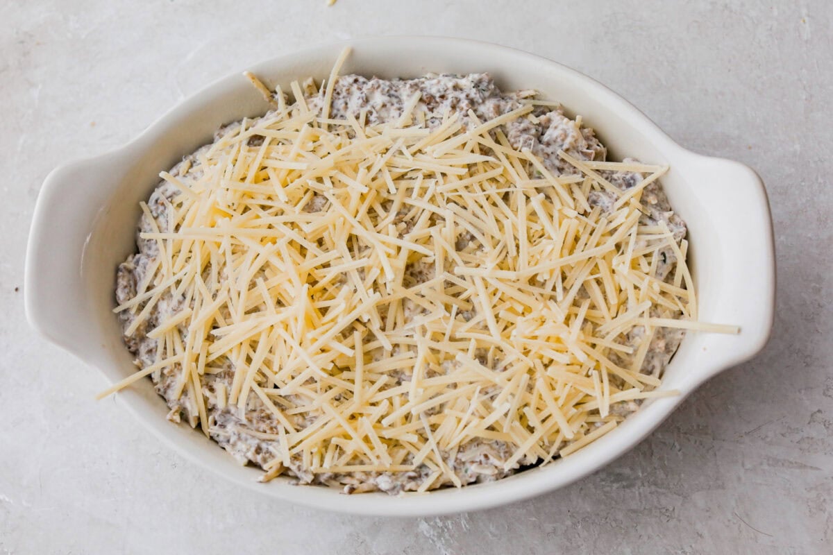Trust me, this Stuffed Mushroom Dip is way easier (and honestly better) than making stuffed mushrooms. You skip all the filling and baking but still get that creamy, cheesy, herby, sausage flavor everyone’s obsessed with. Dip ingredients layered in a baking dish.