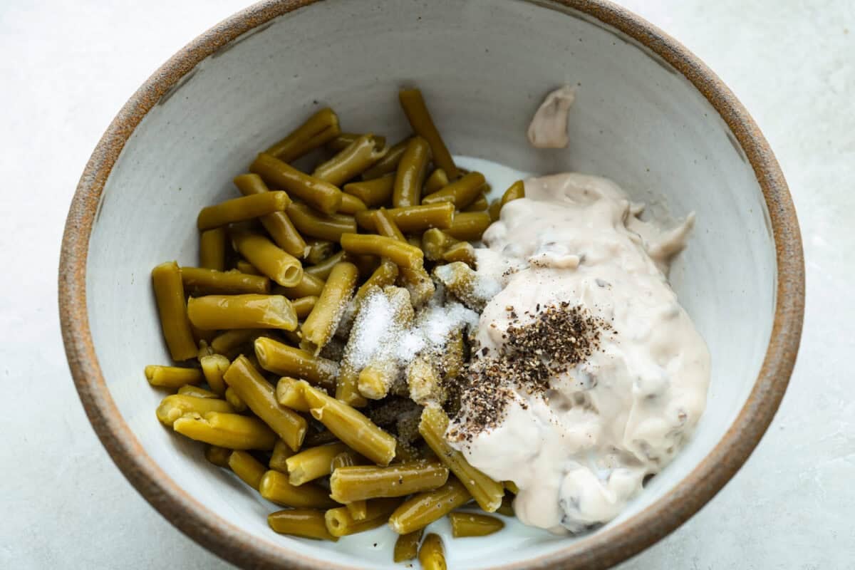 Thanksgiving doesn’t have to mean a long grocery list or an expensive spread. This 5-ingredient green bean casserole keeps things simple, affordable, and classic. It’s proof that comfort food doesn’t need a dozen ingredients. Beans, soup, salt, and pepper added to a mixing bowl.