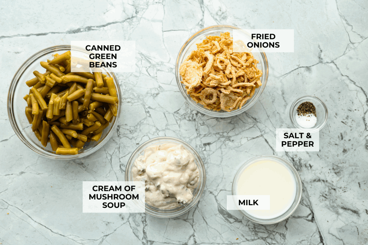 Thanksgiving doesn’t have to mean a long grocery list or an expensive spread. This 5-ingredient green bean casserole keeps things simple, affordable, and classic. It’s proof that comfort food doesn’t need a dozen ingredients. Overhead shot of labeled 5 ingredients green bean casserole ingredients.