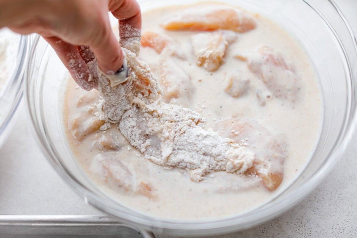 Breaded chicken tender being dipped back into the marinade for a second coating.