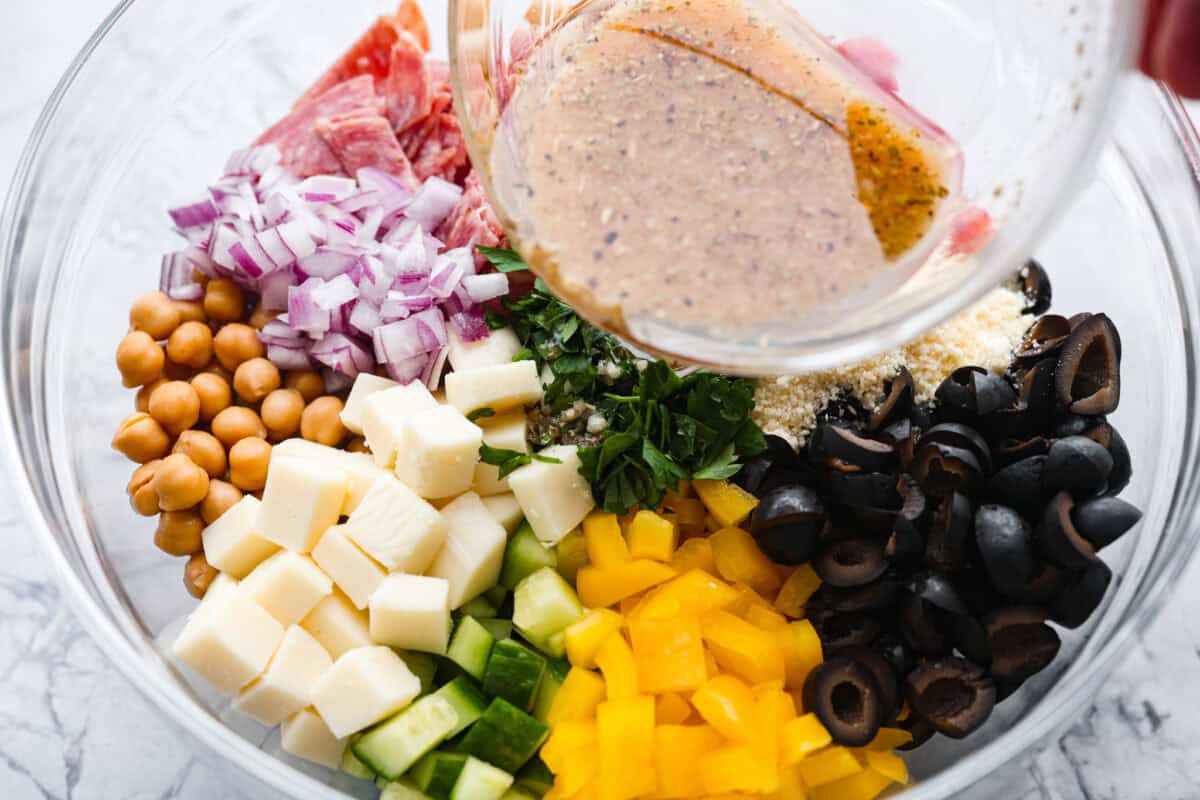 TikTok creator Violet Witchel made this dense bean salad go viral for good reason. It’s simple, high in fiber, protein-packed, and stays delicious for days. My version keeps the same hearty texture and zesty flavor that made her trend explode. Someone pouring the dressing over the large bowl of salad ingredients.