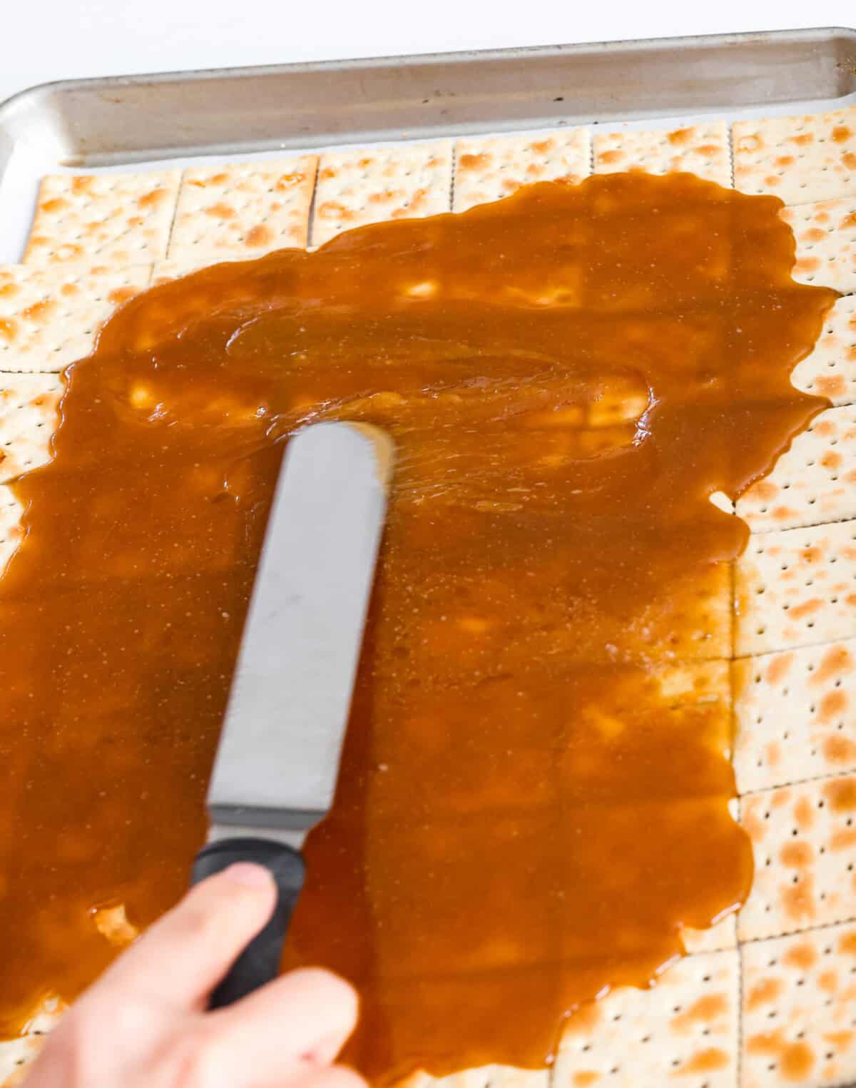 If you want a quick, crunchy treat with a bit of holiday mischief, this Grinch Christmas Crack is it. Sweet, salty, and totally addictive. My classic Christmas Crack is always a hit, but this version brings all the Grinchy fun! Someone gently spreading toffee over the saltine crackers.