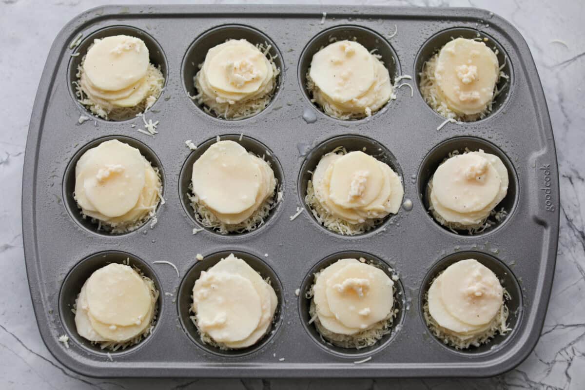 My crispy potato stacks take everything you love about cheesy, golden potatoes and turn it into an easy side dish. Thin slices bake into crisp edges and tender centers, with melty cheese and dripping with seasoned garlic butter! Potato slices stakced in a muffin tin with the butter sauce and cheese in between the layers.