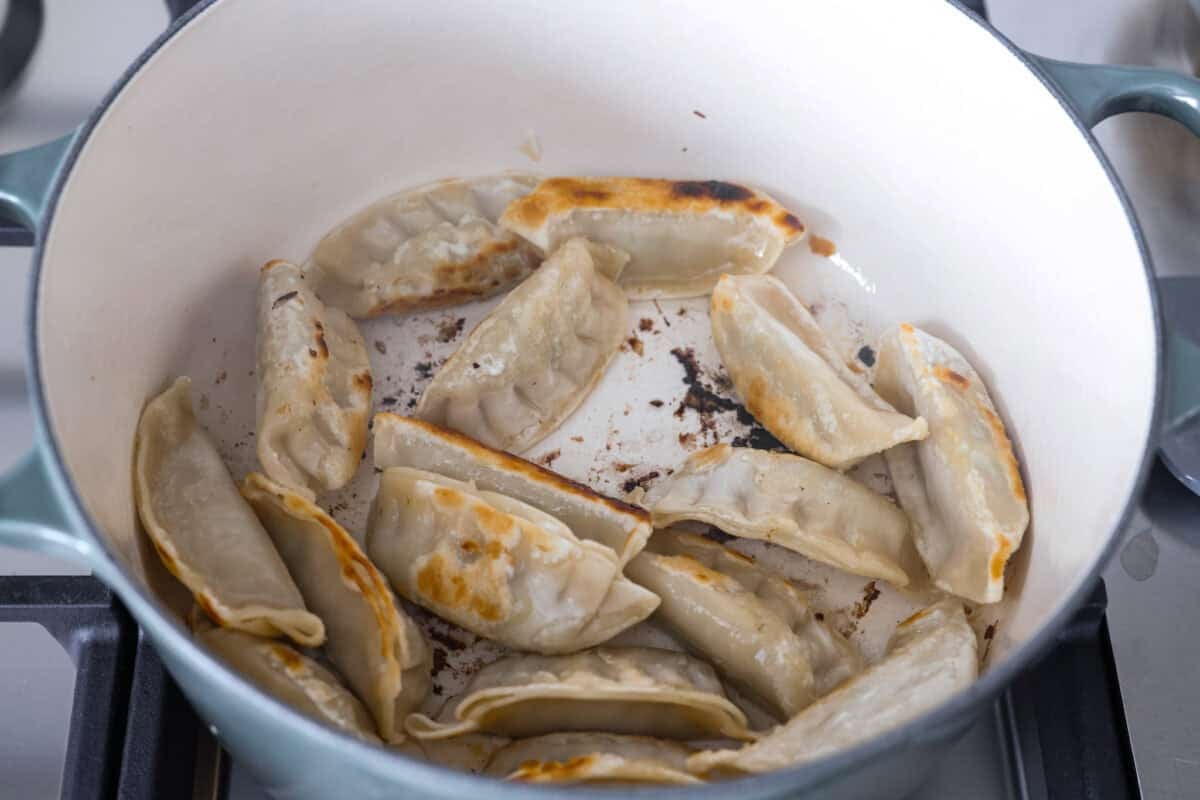 My potsticker soup is what you make when you’re busy, hungry, and need something quick that still tastes really good. All it takes is some frozen potstickers, a simple broth, and a handful of veggies! Potstickers crisping up in a pot on the stove.