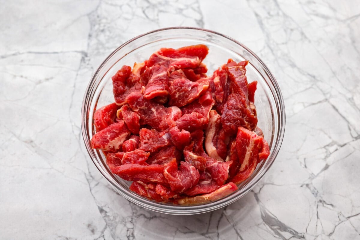 Beef covered in cornstarch and soy sauce sitting in a bowl to marinate. 