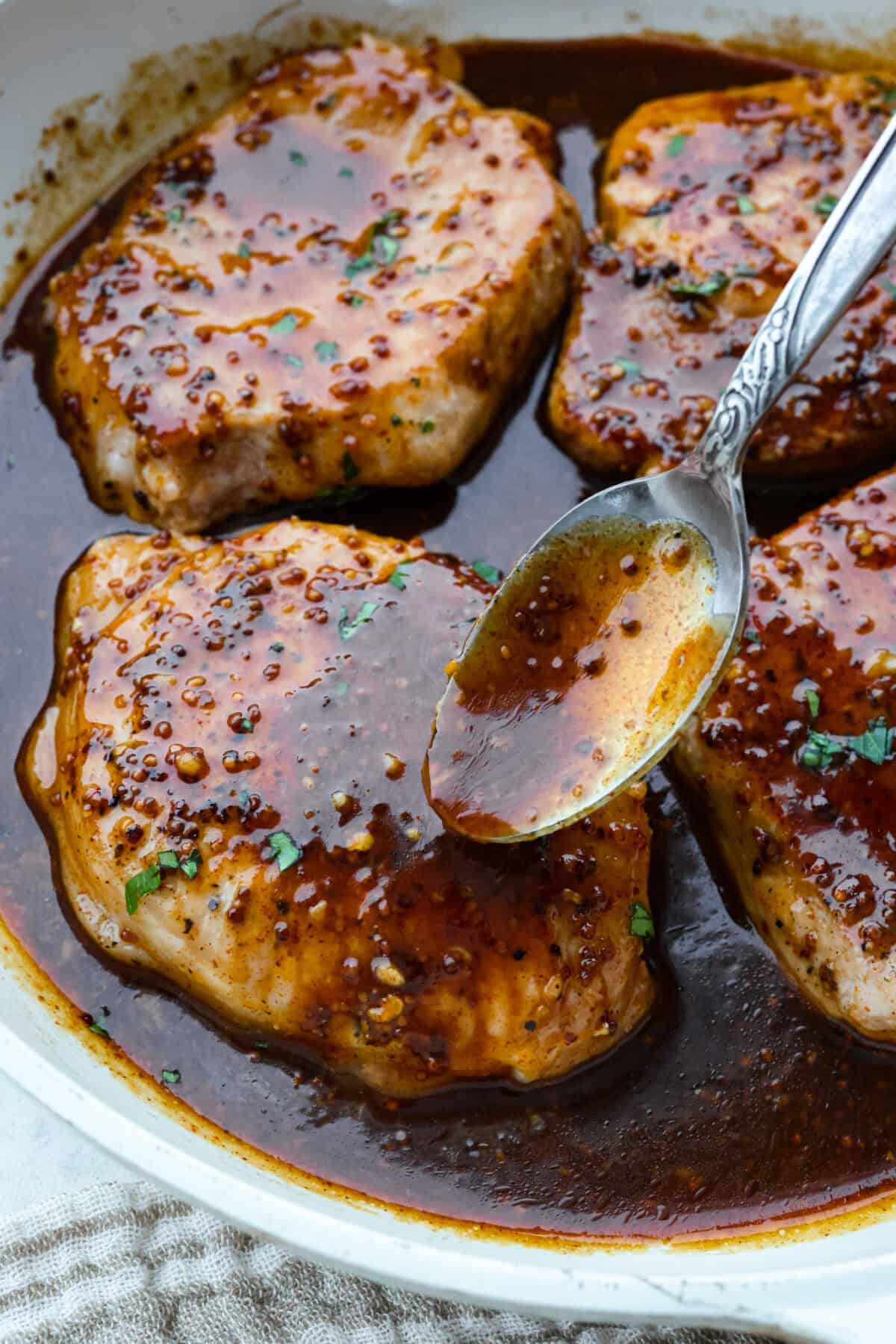 These honey mustard pork chops bring big flavor with very little effort. The whole grain mustard adds texture and bite, while a few extra spices deepen the sauce, turning a simple skillet dinner into something totally crave-worthy. Close up of someone spooning honey mustard sauce over the pork chops.