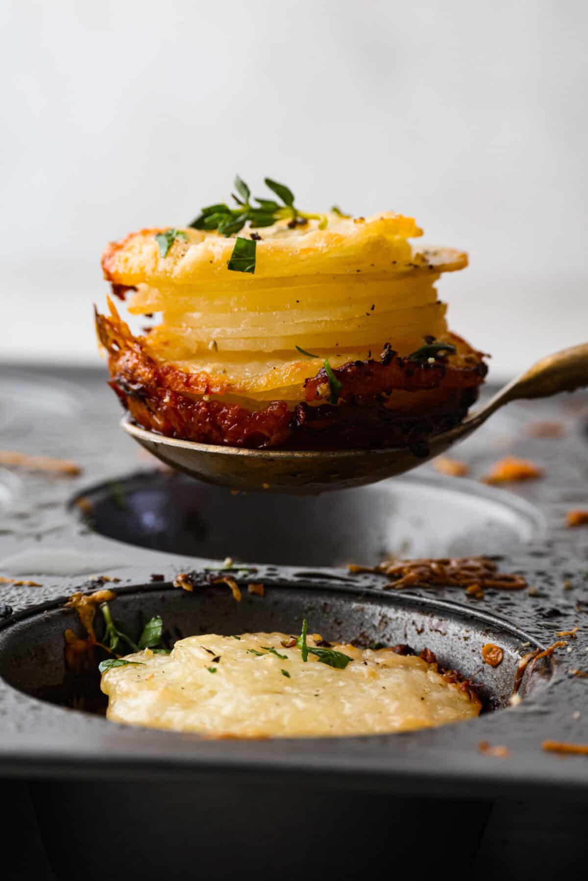 My crispy potato stacks take everything you love about cheesy, golden potatoes and turn it into an easy side dish. Thin slices bake into crisp edges and tender centers, with melty cheese and dripping with seasoned garlic butter! Someone lifting a potato stack out of the muffin tin.