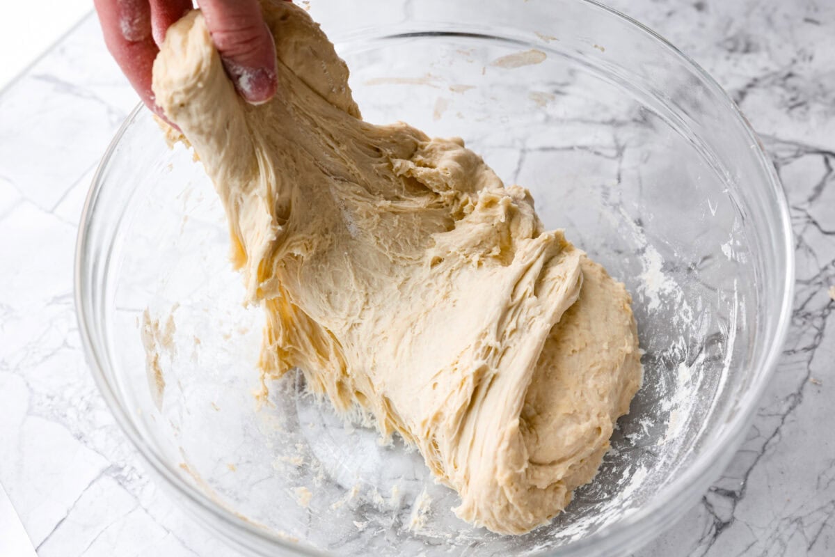 Myย 4-ingredient artisan breadย is simple, rustic, and completely bakery-worthy. With just flour, water, yeast, and salt, youโll get a loaf with a crusty outside and a soft, chewy center. Someone stretching another side of the dough ball ready to fold it over the whole dough ball.