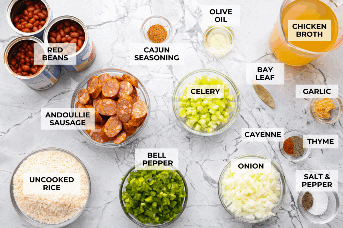 If your family is hungry now and you don't have time to soak beans or babysit the stove, this red beans and rice is for you. It is quick, cozy, and made with canned beans and smoky sausage. It tastes great and is ready fast! Overhead shot of labeled red beans and rice ingredients.