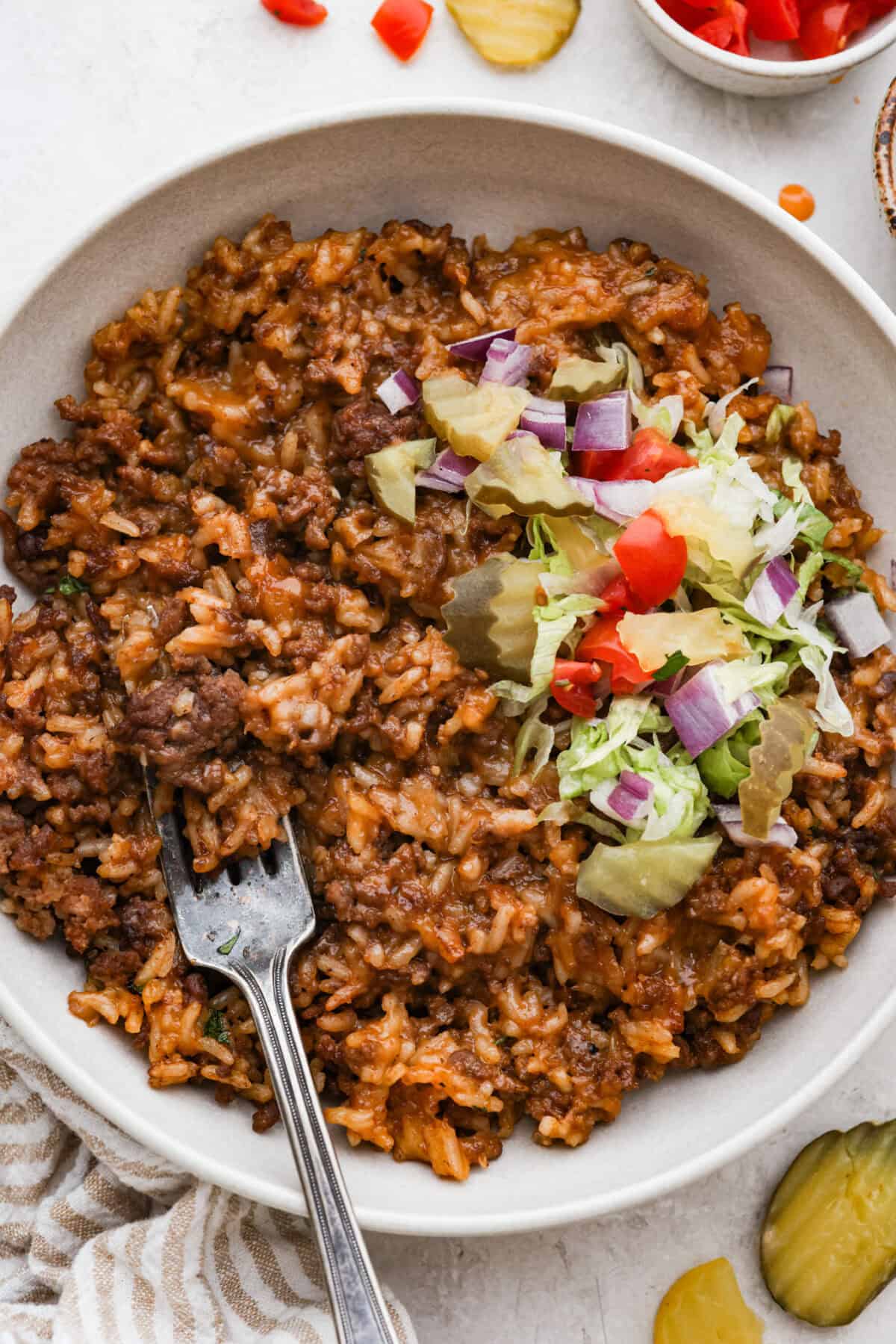 Bowl of cheeseburger rice topped with lettuce, onion, tomato, lettuce and pickle.