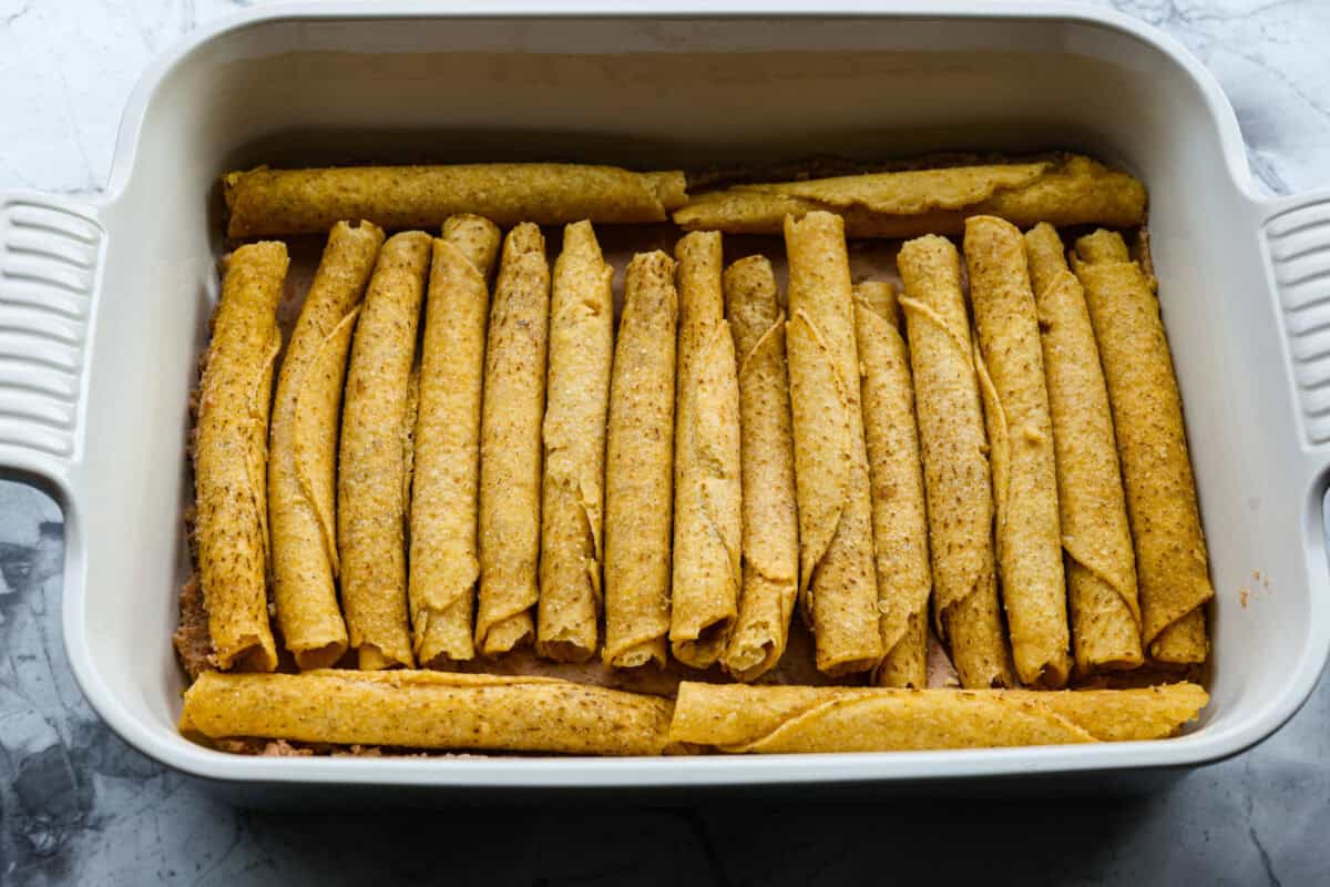 Taquitos layered on top of the refried beans in the baking dish. 