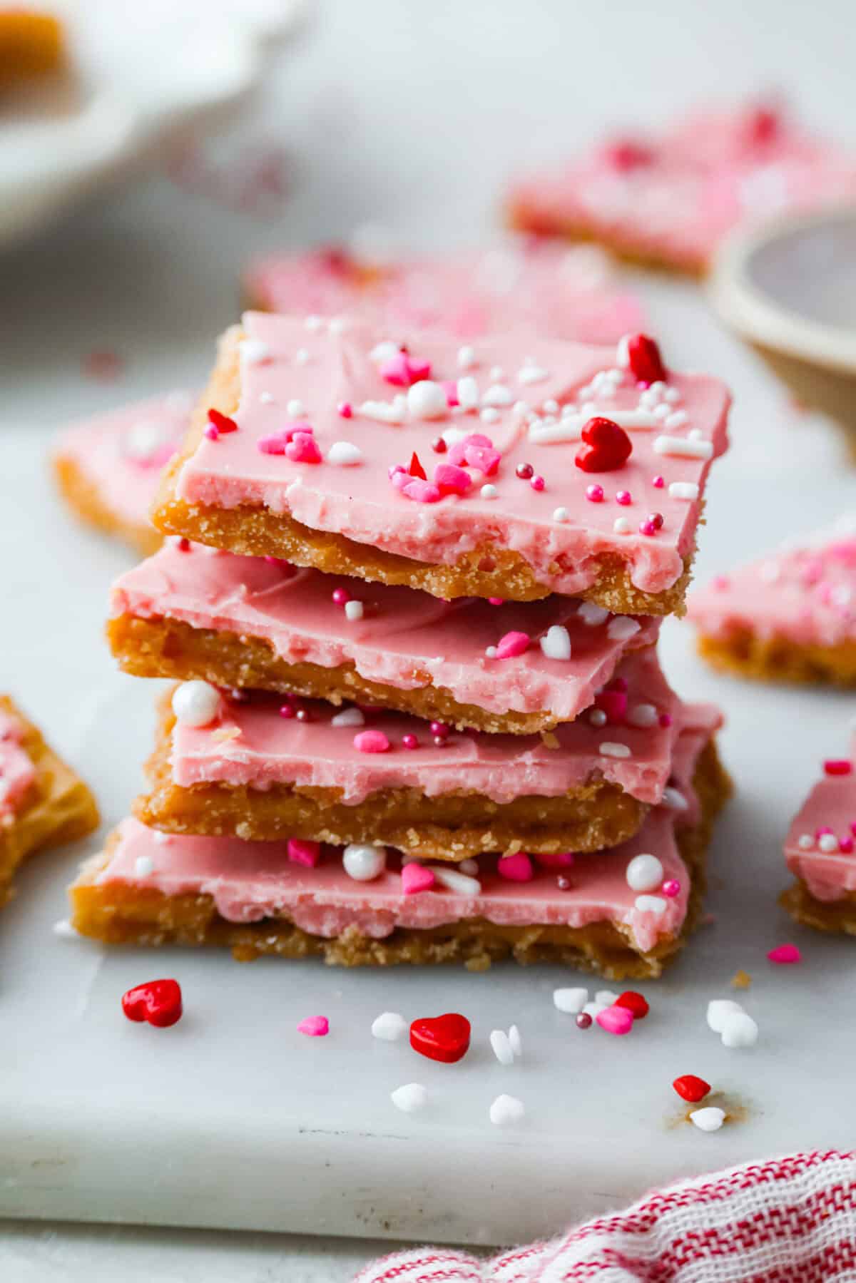 My Valentine’s Day Crack is the cutesy pink version of my famous Christmas crack! Same buttery, snappy toffee base, just with pink candy melts and festive sprinkles. It's perfect for kids' parties, Galentine's, or a sweet little Valentine's treat. Stack of pieces of Valentine's day crack.