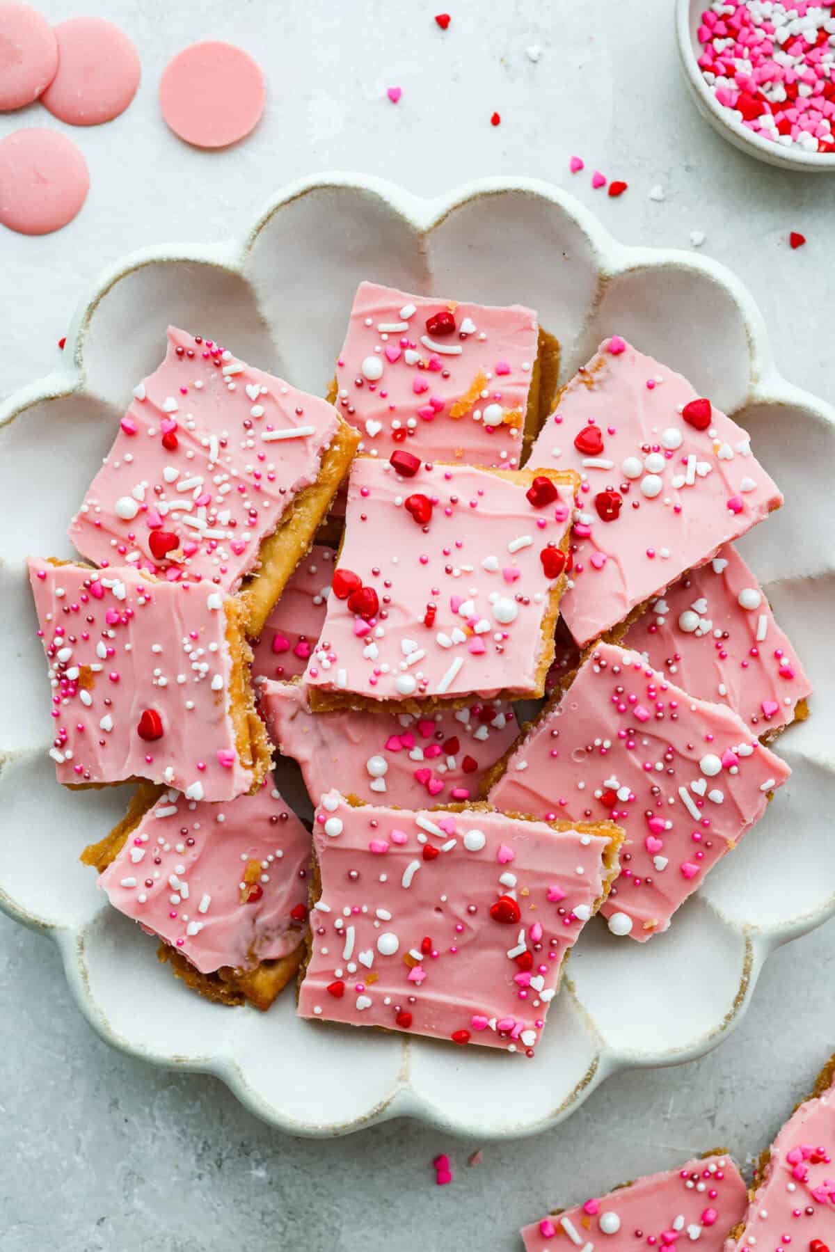 My Valentine’s Day Crack is the cutesy pink version of my famous Christmas crack! Same buttery, snappy toffee base, just with pink candy melts and festive sprinkles. It's perfect for kids' parties, Galentine's, or a sweet little Valentine's treat. Serving plate piled with pieces of Valentines day crack.