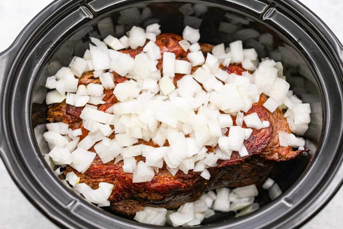 This horseradish pot roast is pure comfort food with a flavorful twist. The beef cooks low and slow until fork-tender, soaking up a rich, savory sauce with just enough horseradish to add depth without being overwhelming. Browned pot roast in the slow cooker with diced onions.