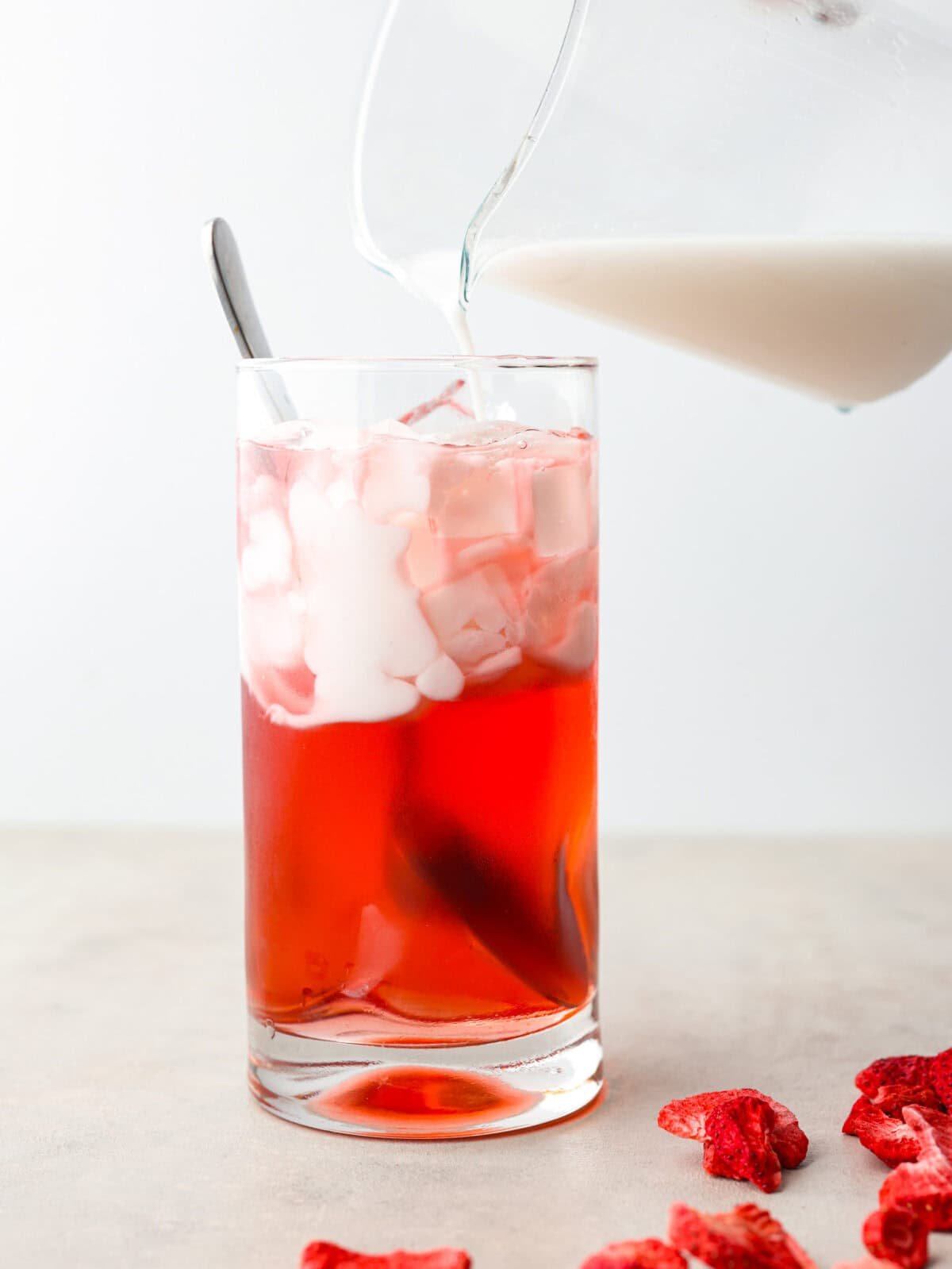 You guys, Starbucks sells the Strawberry Açaí concentrate in stores! Which means we can make the famous Starbuck's Pink Drink at home! And let me tell you, it's spot on! With just three ingredients, it's ridiculously easy to make year-round, and so good! Someone pouring coconut cream into a glass with strawberry acai concentrate.