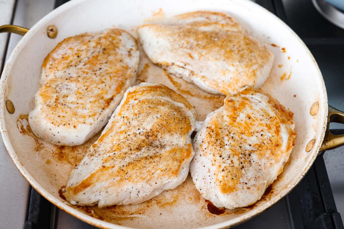 This chicken Diane takes everything you love about steak Diane and turns it into an easy chicken dinner. One skillet, a rich creamy mushroom sauce, and tons of flavor in every bite! Chicken breasts cooking in a skillet.