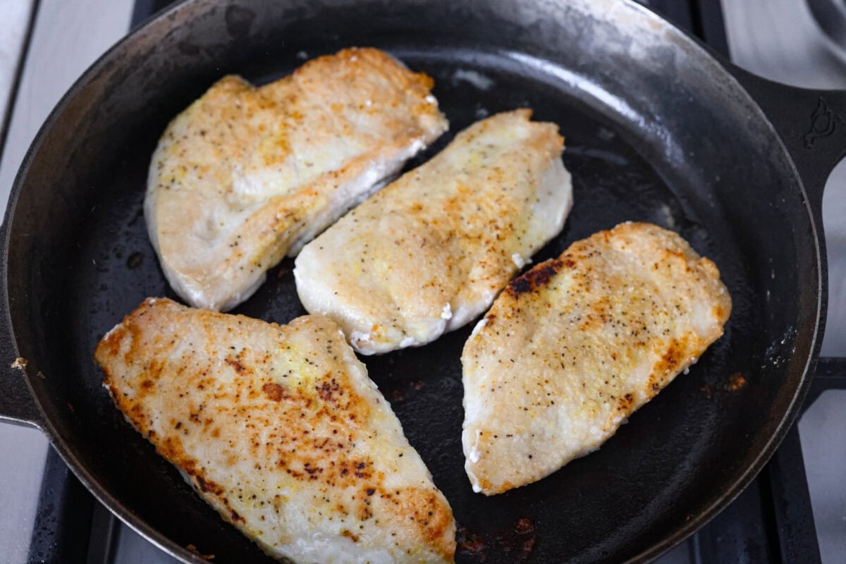 This lemon butter chicken is about to become your new weeknight secret weapon. One skillet, simple ingredients, and less than 30 minutes to the most golden, saucy, creamy chicken you've ever made. Chicken breasts cooking in a skillet.