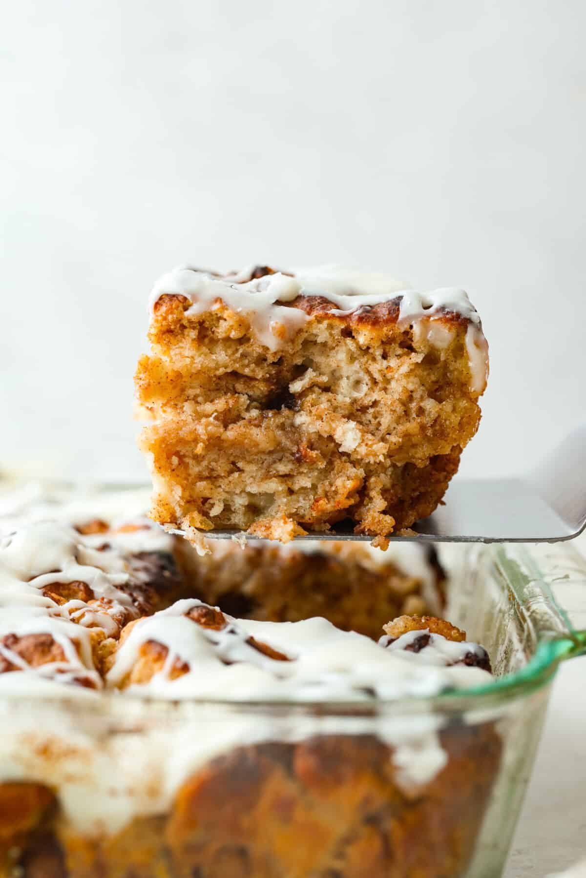 These cinnamon roll butter swim biscuits are my cheat code to making "cinnamon rolls." They bake up soft and fluffy with a sweet cinnamon swirl and icing on top. They disappear almost as fast as you can make them! Someone lifting a slice of the cinnamon roll butter swim biscuits out of the pan.