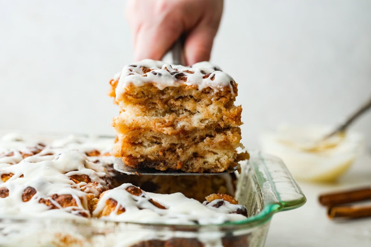 These cinnamon roll butter swim biscuits are my cheat code to making "cinnamon rolls." They bake up soft and fluffy with a sweet cinnamon swirl and icing on top. They disappear almost as fast as you can make them! someone lifting a piece of cinnamon roll butter swim biscuit out of the pan.