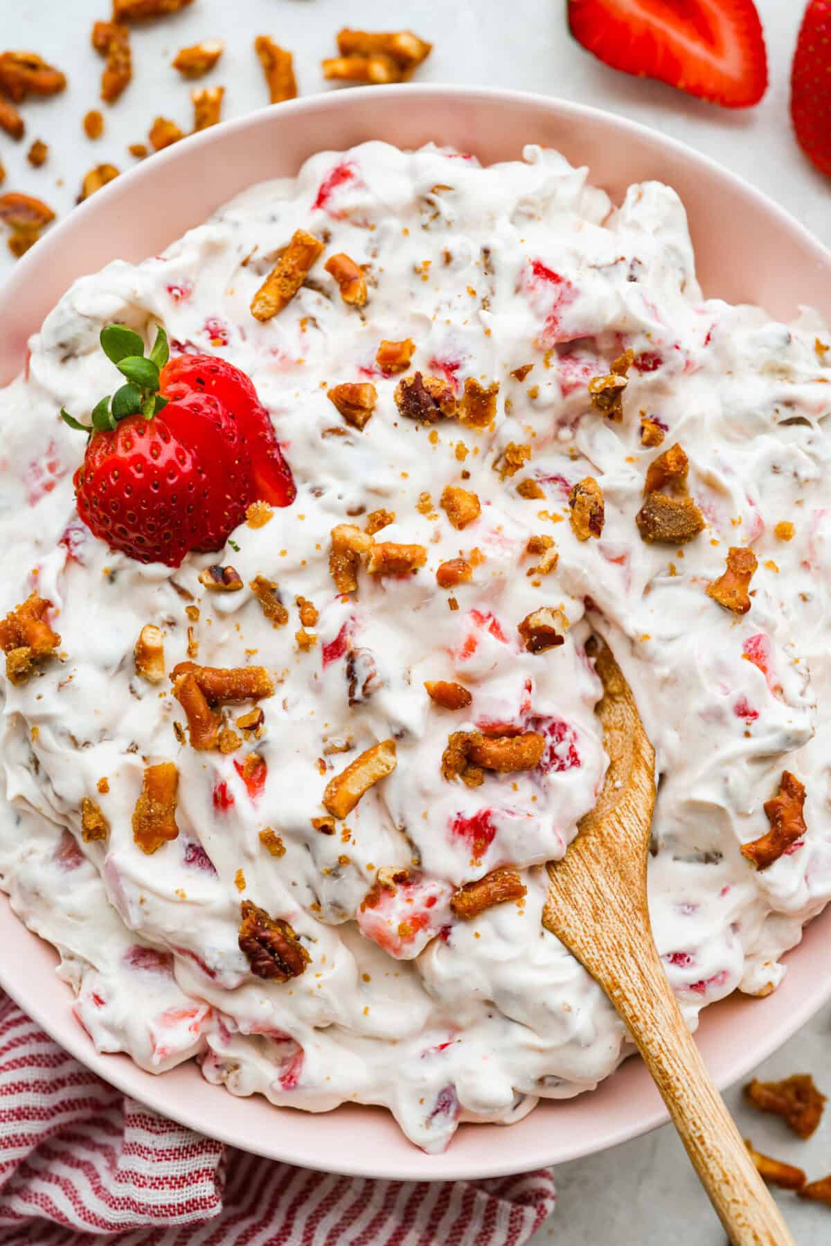A large bowl of crack pretzel salad with a wooden spoon and garnished with strawberries.