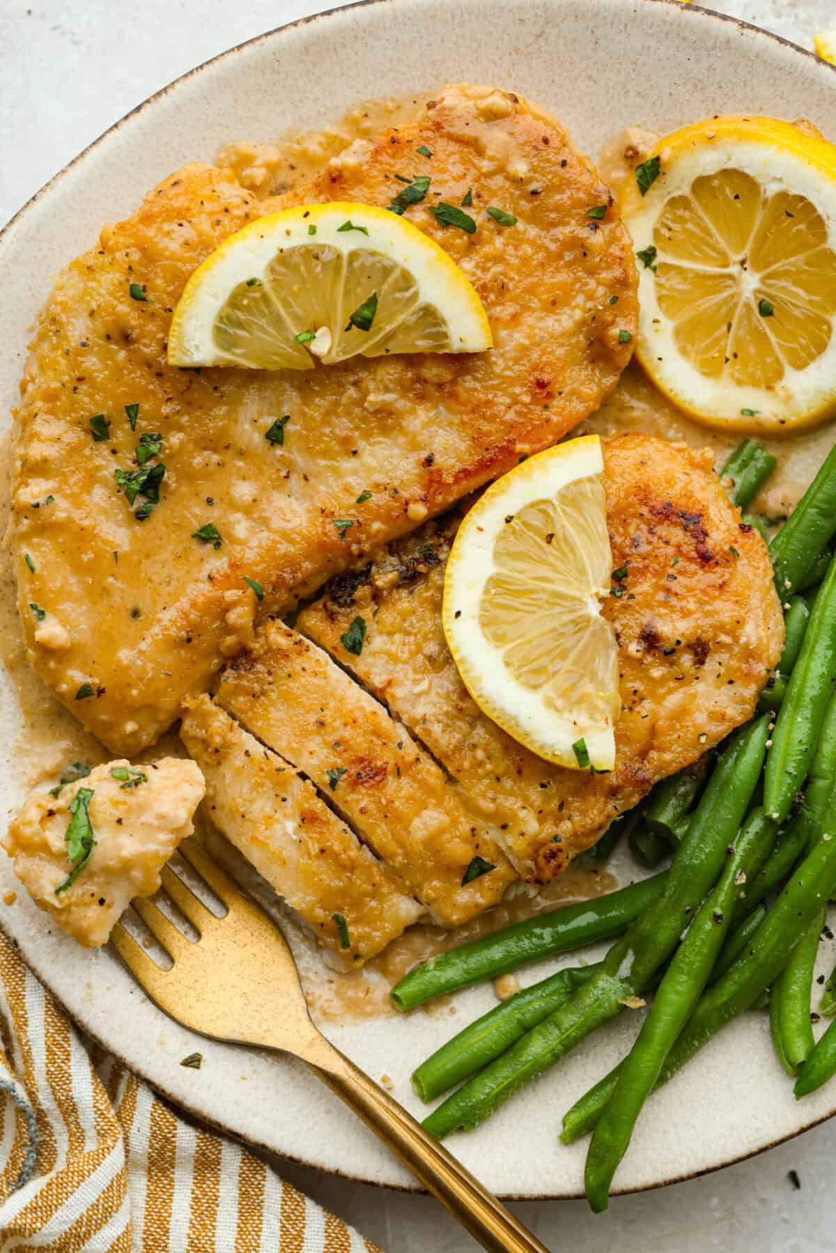 This lemon butter chicken is about to become your new weeknight secret weapon. One skillet, simple ingredients, and less than 30 minutes to the most golden, saucy, creamy chicken you've ever made. Plated lemon butter chicken garnished with lemon slices with a side of green beans.