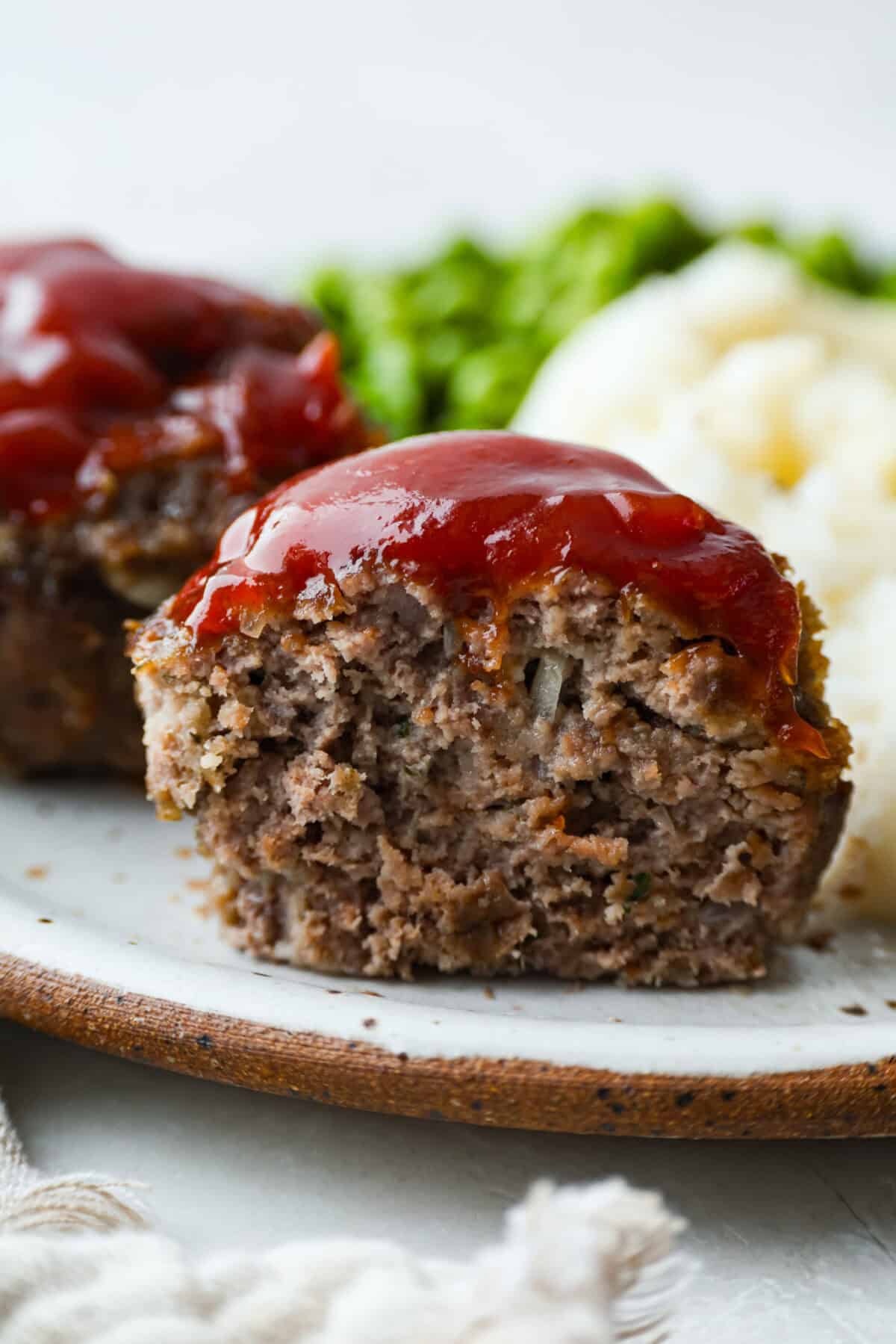 Meatloaf is even better in mini form! These mini meatloaf muffins are tender, flavorful, and topped with a sweet, tangy glaze. They are done in about 25 minutes, making them perfect for an easy dinner I know the kids will love. Mini meatloaf cut through the center vertically so you can see al the juicy meat and onions and tangy glaze on top.