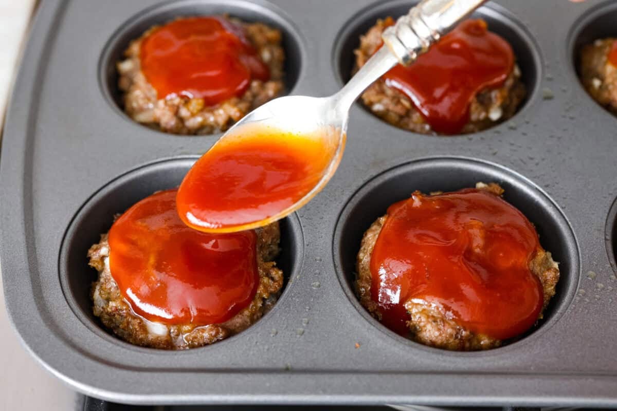Meatloaf is even better in mini form! These mini meatloaf muffins are tender, flavorful, and topped with a sweet, tangy glaze. They are done in about 25 minutes, making them perfect for an easy dinner I know the kids will love. Glaze being spooned over the mini meatloaf muffins.