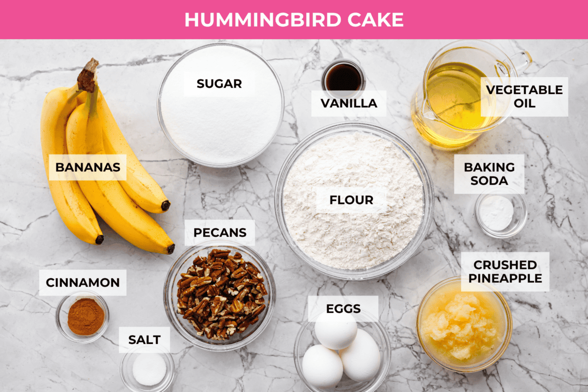 If youโve never had hummingbird cake, just know itโs one of those cakes people take a bite of and immediately ask for the recipe. Itโs soft, sweet, packed with banana and pineapple, and topped with a cream cheese frosting that is to die for! Overhead shot of labeled hummingbird cake ingredients.