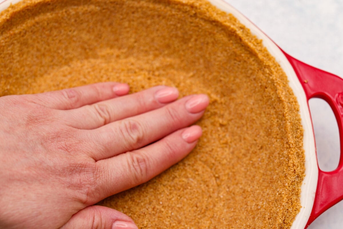 Someone smashing the crust ingredients into the bottom of the pie dish. 