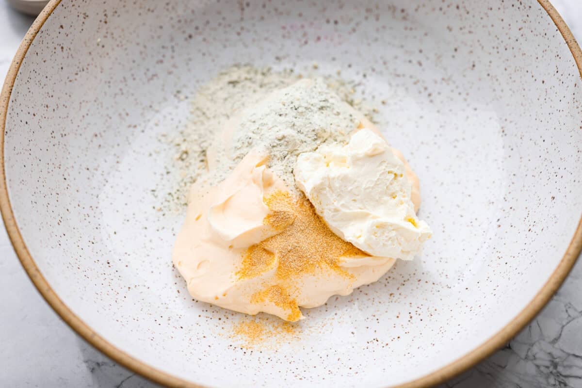 Cream cheese, mayo, garlic and ranch seasoning all added to a mixing bowl.