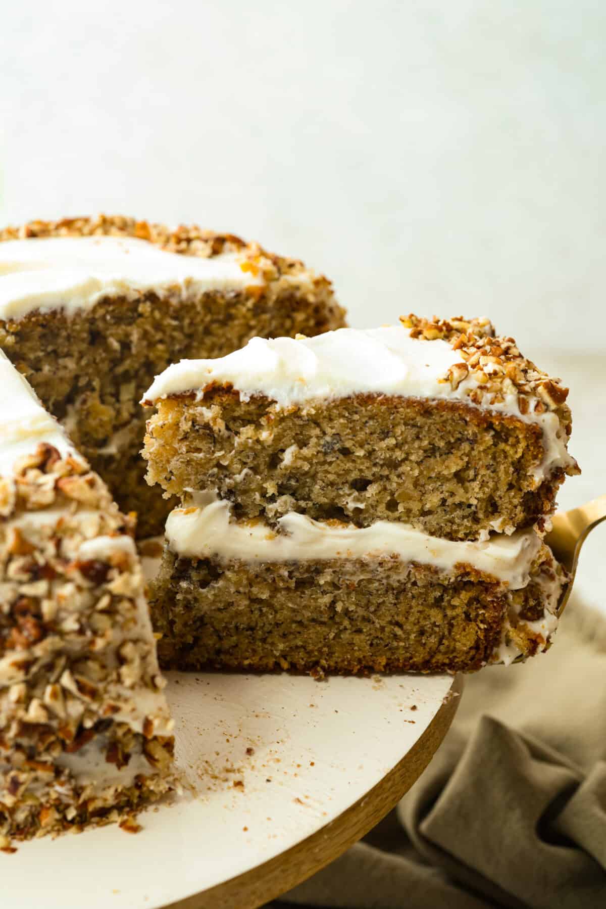 If youโve never had hummingbird cake, just know itโs one of those cakes people take a bite of and immediately ask for the recipe. Itโs soft, sweet, packed with banana and pineapple, and topped with a cream cheese frosting that is to die for! Slice of hummingbird cake being taken out of the cake.