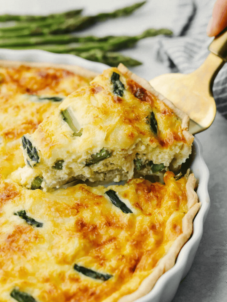someone lifting out a slice of asparagus quiche. 