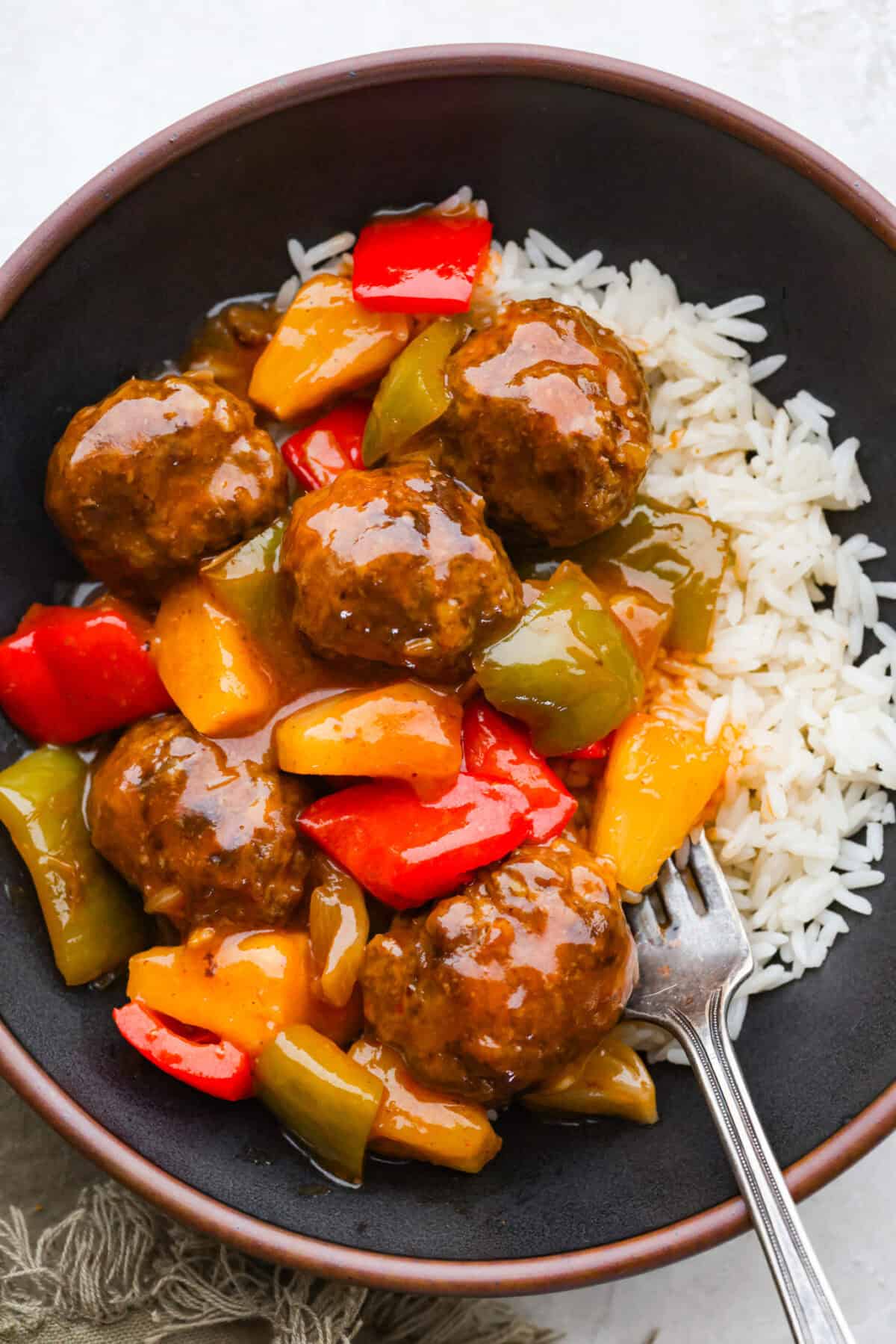 These sweet and sour meatballs are one of those dinners I pull out when I need something easy, but I know everyone likes! They’re saucy, a little sweet, a little tangy, and come together fast. Bowl with a serving of sweet and sour meatballs on a bed of rice.