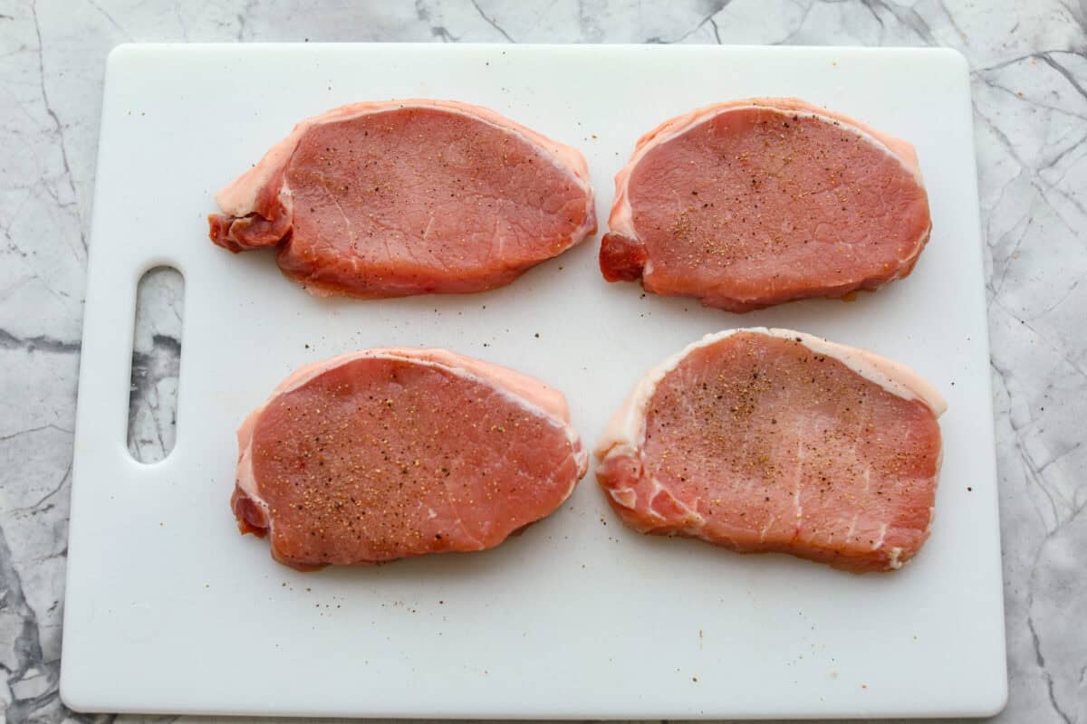 Pork chops seasoned and resting on a cutting board. 