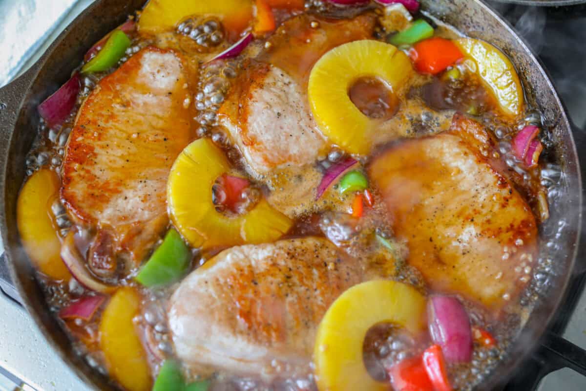 Pork chops, veggies and pineapples added to the sauce in the skillet to continue to cook.