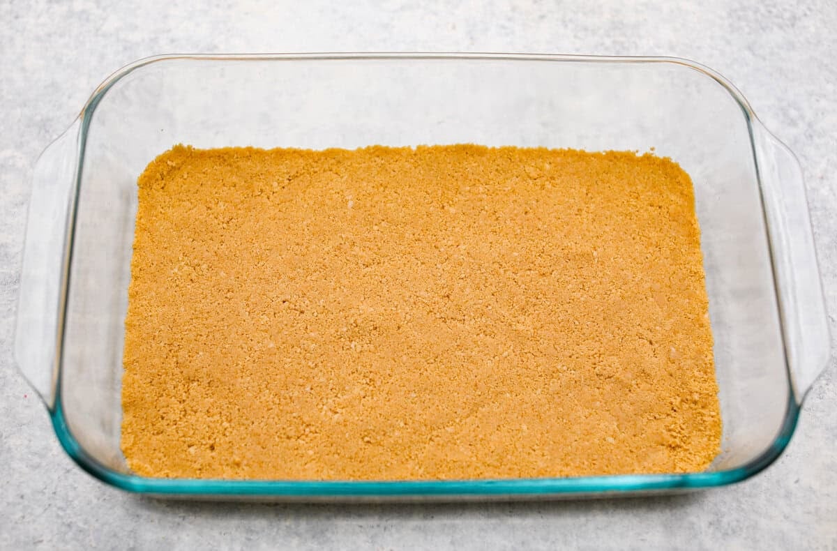 Orange creamsicle lush is sunshine in dessert form! With creamy orange layers, a buttery golden Oreo crust, and bright fresh citrus flavor, this easy no-bake dessert is a fun twist on my popular Lemon Lush that’s perfect for summer. Cookie crust in the bottom of a 9x13 pan for the orange creamsicle lush dessert.