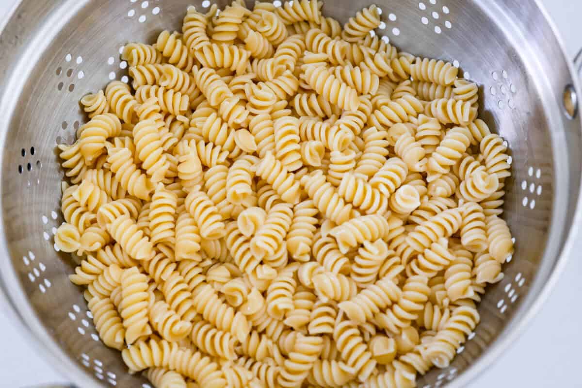 Pizza pasta salad is a fun twist on two family favorites! It's packed with pepperoni, mozzarella, fresh veggies, and a tangy pizza-inspired dressing. Get out of your pasta salad rut and make this unique and incredibly flavorful recipe! Cooked pasta in a colander.
