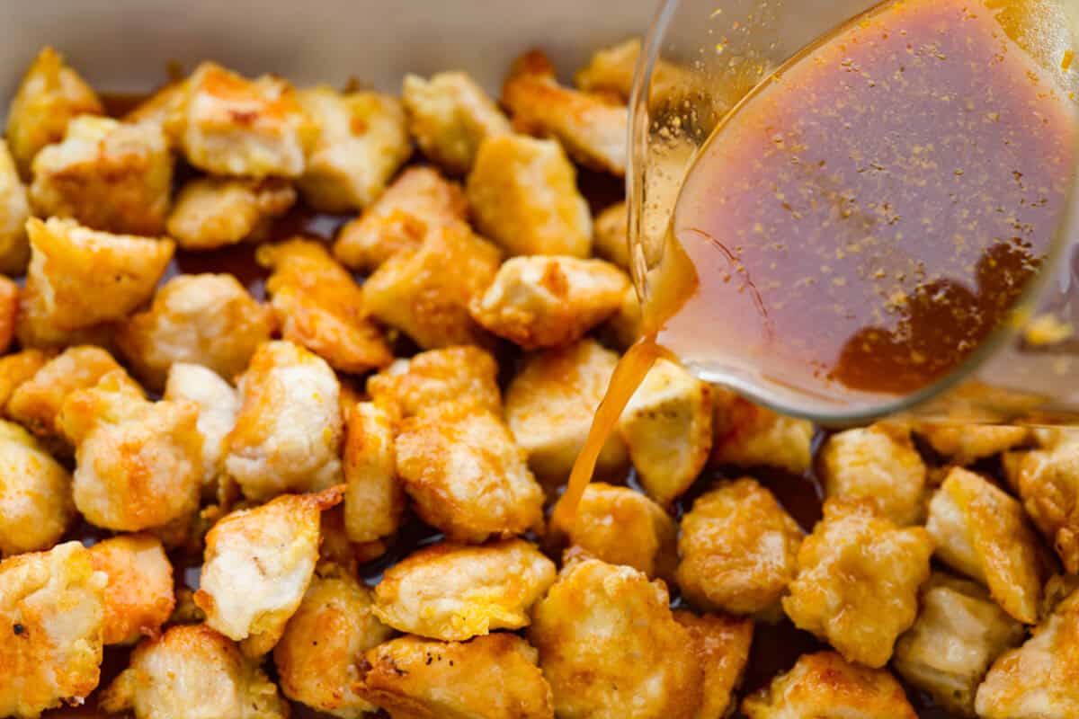 Baked orange chicken is sweet, tangy, and coated in the best sticky orange sauce. It has all the flavor of your favorite takeout, but itโs made right at home and baked until the chicken is perfectly tender. Someone pouring the sauce over pan fried chicken pieces before it gets baked.
