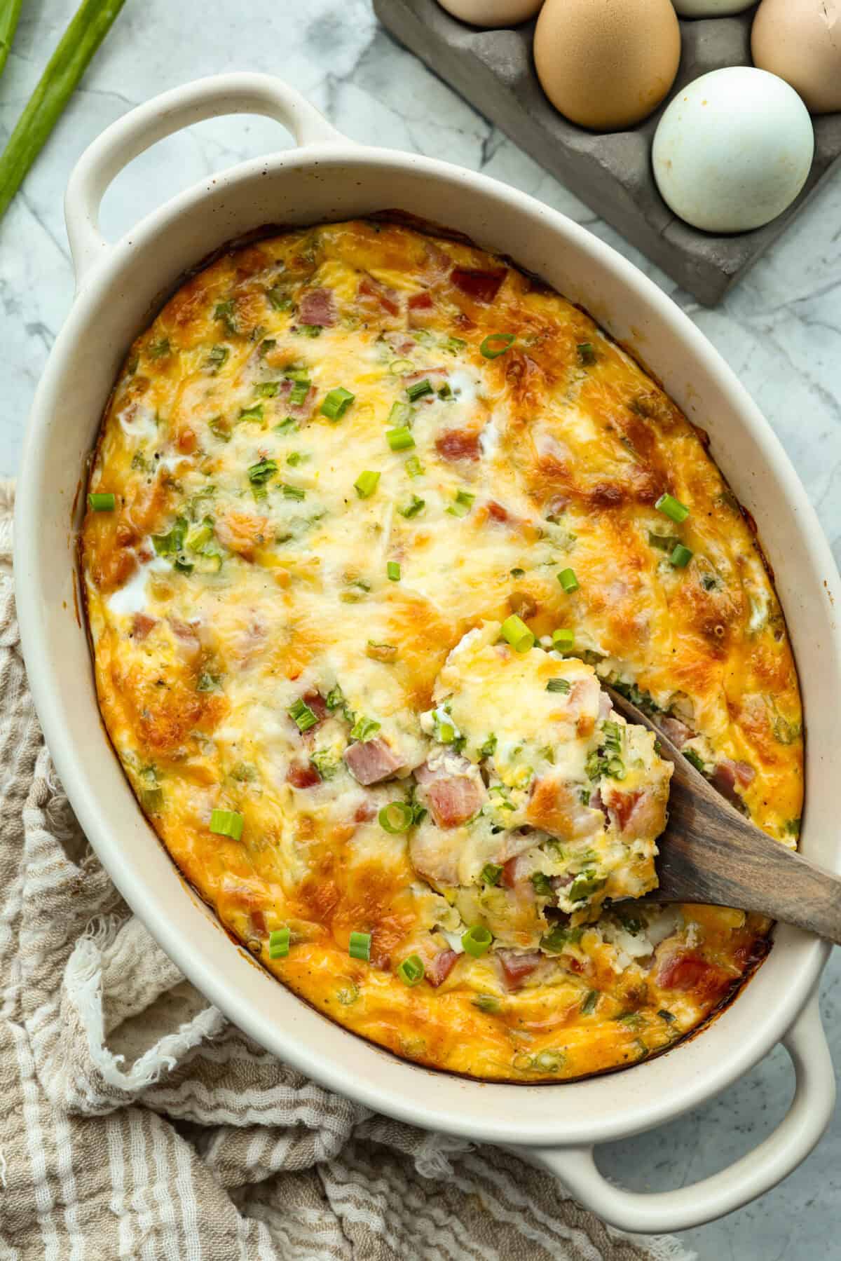 This farmer's casserole is my answer to summer mornings when the kids want cereal again, but I want them to eat something that will actually keep them full. Itโs packed with protein, and it's easy to customize with fresh garden veggies. Baked farmer's casserole with a wooden spoon scooping out a serving.