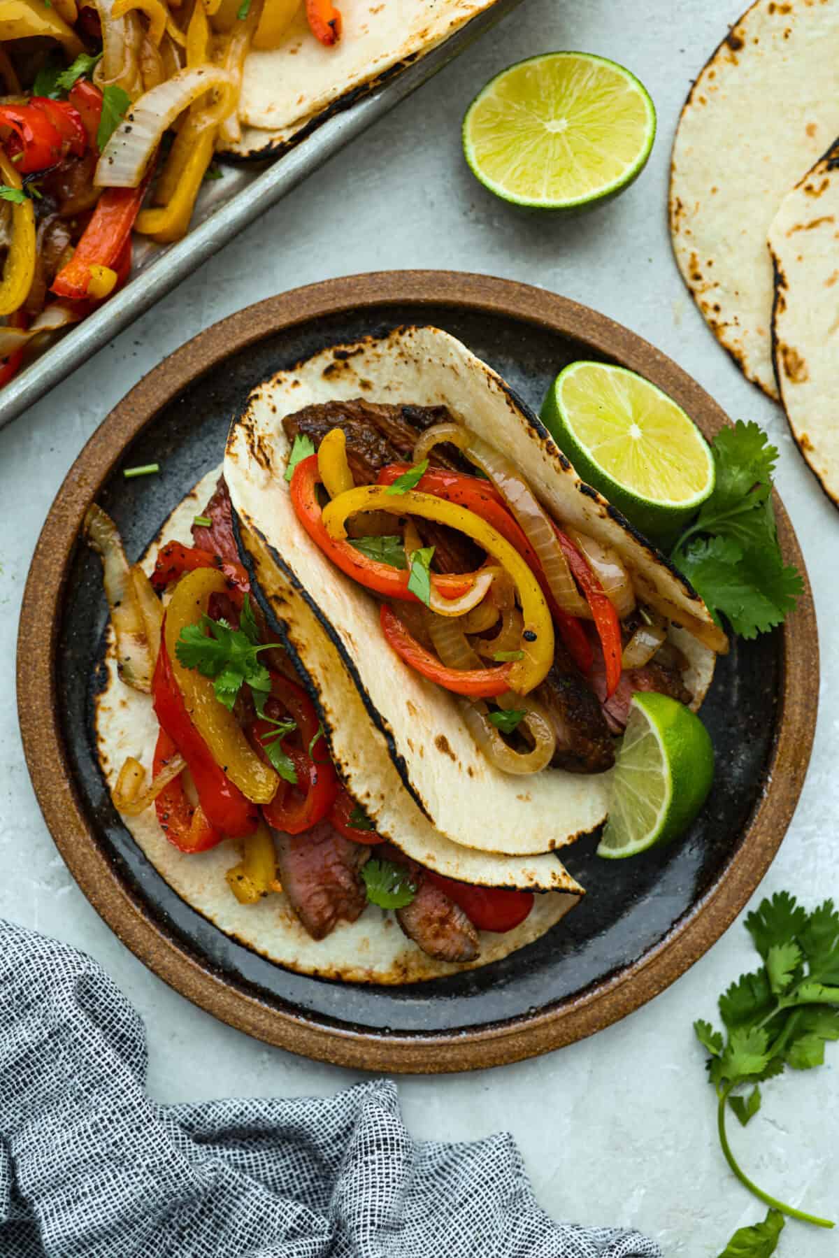 Grilled steak fajitas are one of those dinners that feels fun the second it hit the table. The steak is juicy and smoky, the peppers and onions are tender and flavorful, and everyone gets to build their fajitas just the way they like them. Plate with two tortillas filled with grilled steak fajita ingredients.