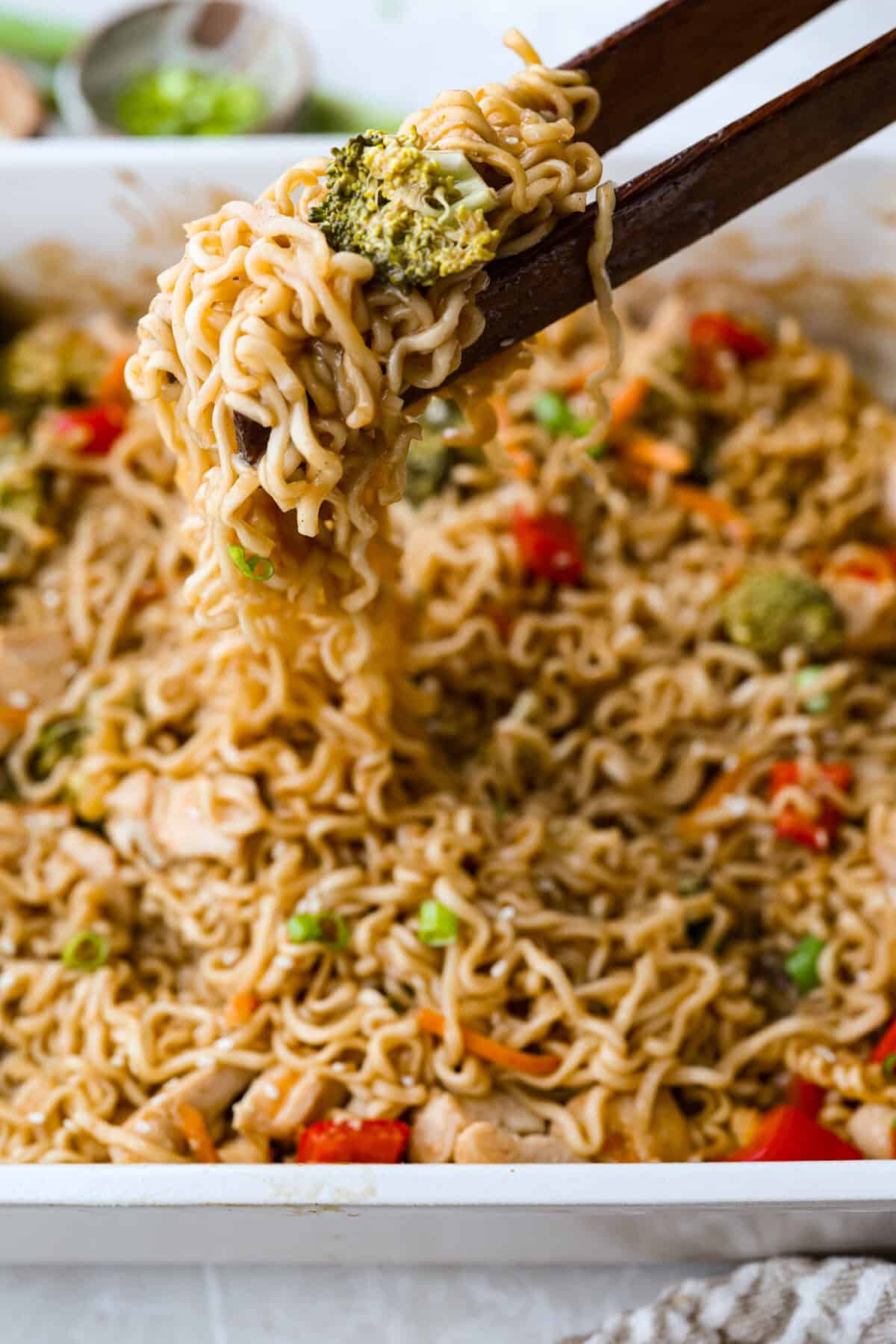 Someone lifting a bite of dump and bake ramen out of the baking dish with chopsticks. 