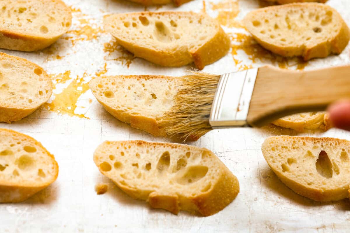 Iโve loved homegrown tomatoes since I was a kid, and this easy bruschetta recipe is one of my favorite ways to use them. The fresh basil, garlic, olive oil, and crispy toasted bread with that balsamic glaze make such a good flavor! Sliced baguettes being spread with olive oil to broil.