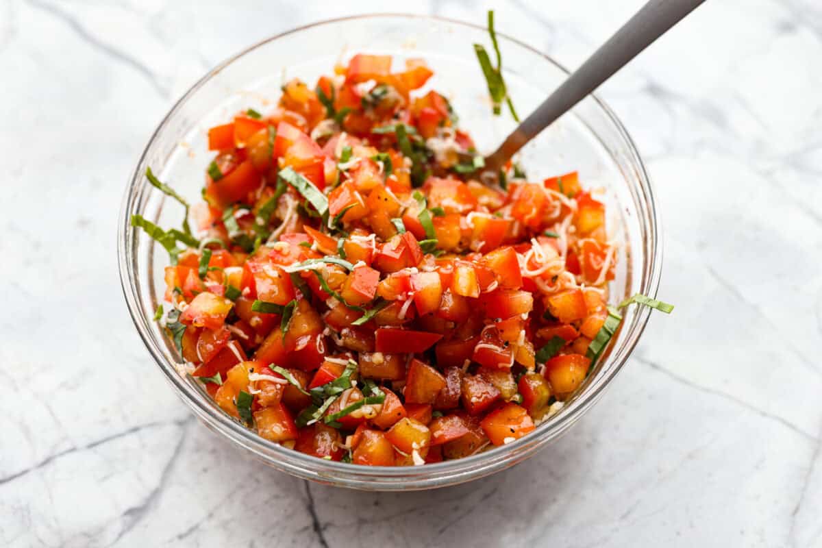 Iโve loved homegrown tomatoes since I was a kid, and this easy bruschetta recipe is one of my favorite ways to use them. The fresh basil, garlic, olive oil, and crispy toasted bread with that balsamic glaze make such a good flavor! All of the ingredients added to a bowl.