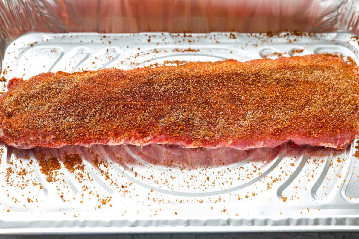 These grilled BBQ ribs are what summer cookouts are all about! Slow-cooked until fall-off-the-bone tender, then finished with a sticky, caramelized layer of BBQ sauce that'll have everyone licking their fingers. Rack of ribs with seasoning rubbed all over it.